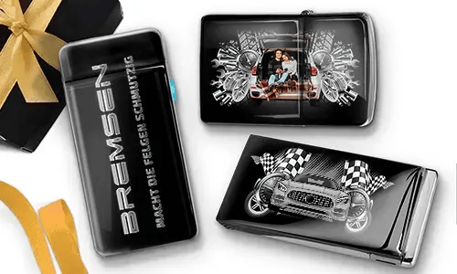 Elegante schwarze Feuerzeuge mit Auto-Designs. Eines zeigt eine Familie in einem Auto, ein anderes ein blaues Auto mit karierten Flaggen. Daneben liegt eine Geschenkbox mit goldener Schleife.