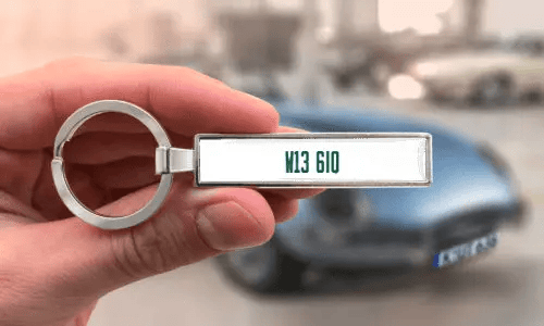Custom license plate keychain held in hand with car in background