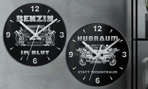 Zwei schwarze Wanduhren mit Autoillustrationen und deutschem Text: BENZIN IM BLUT und HUBRAUM STATT WOHNTRAUM
